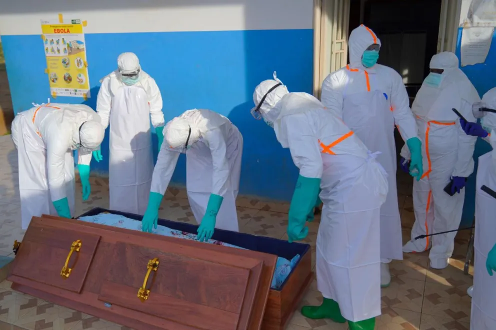 Personal médico con equipo de protección metiendo el cuerpo de una víctima de ébola en un ataúd en Bunia, en la RD del Congo. Foto: EFE/