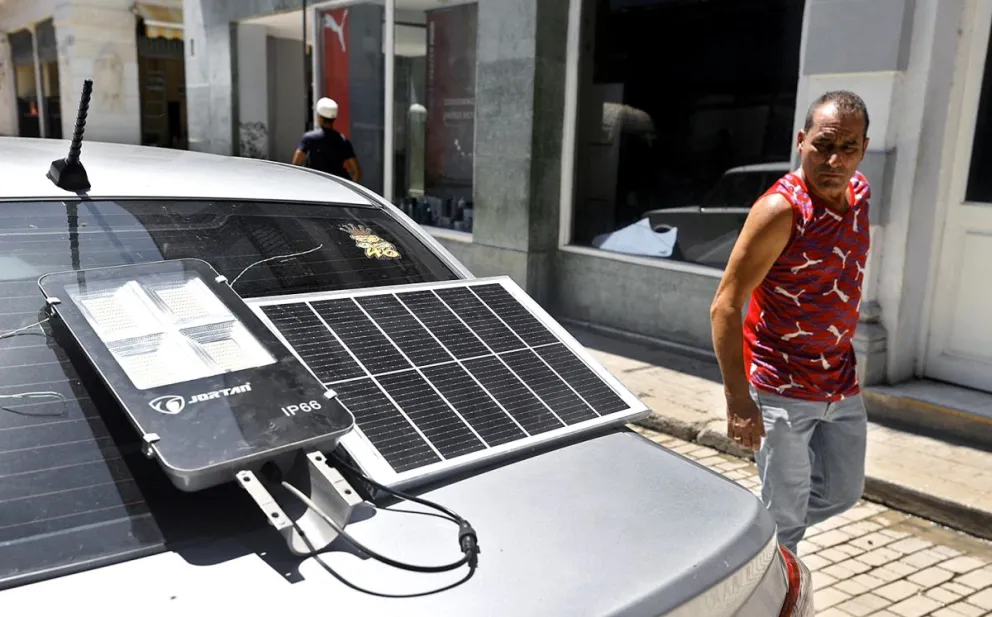 Imagen de archivo en la que se captó a un hombre al observar un panel solar que suministra energía a una lámpara, sobre el baúl de un automóvil, en La Habana (Cuba). Foto: EFE