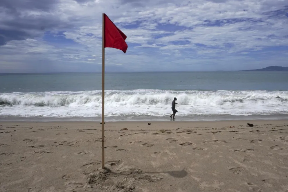 Un hombre camina en la playa cerca de una bandera roja como aviso del fuerte oleaje ante el paso del huracán Rachel en el malecón de Puerto Vallarta (México). Imagen de archivo. EFE/ Arturo Montero