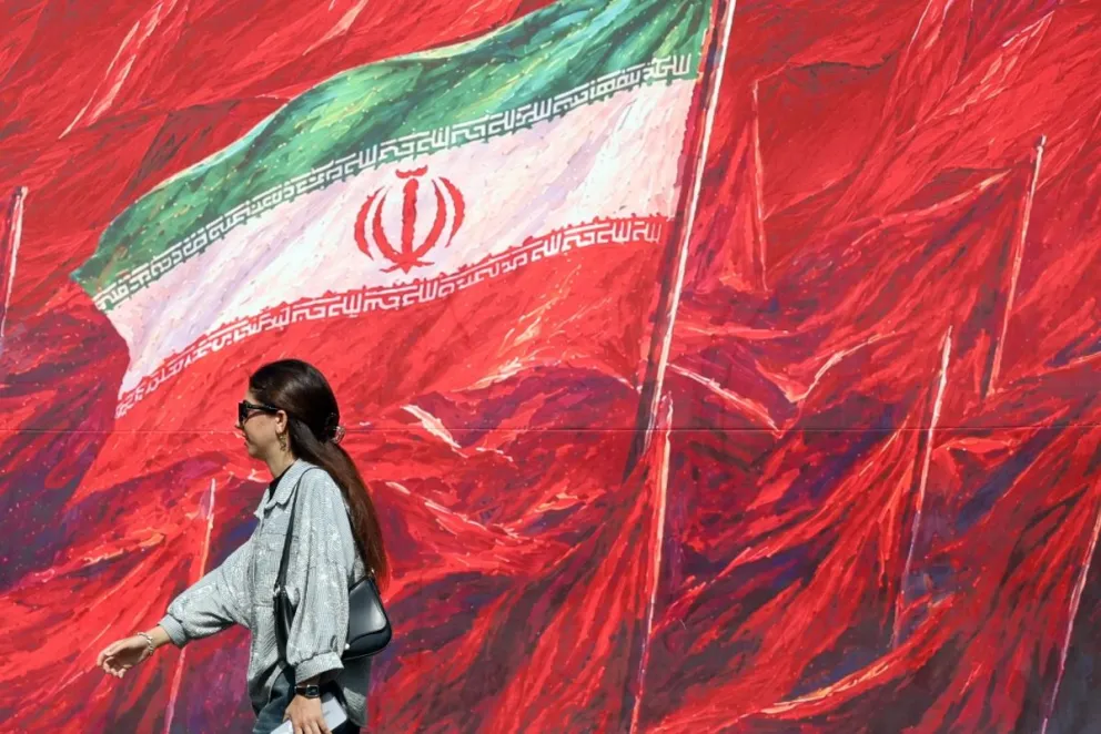 Una mujer iraní pasa junto a una pancarta que muestra la bandera nacional de Irán en una calle de Teherán, Irán, en una imagen del 14 de octubre de 2026. Foto: EFE