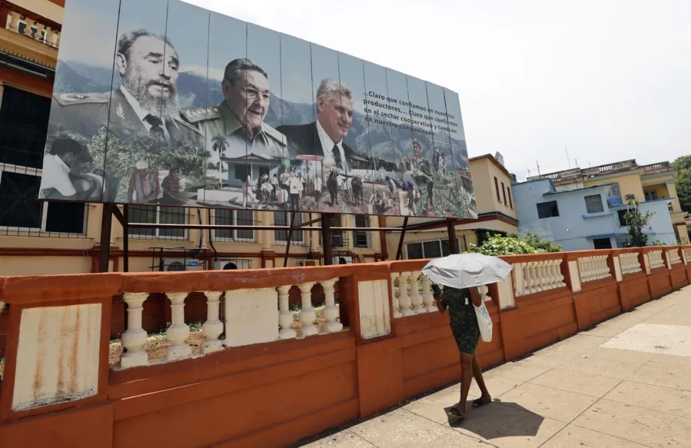 Una mujer camina frente a una valla que muestra las imágenes del presidente de Cuba, Miguel Diaz-Canel (d), el general y expresidente Raúl Castro (c), y el fallecido expresidente de Cuba Fidel Castro (i), en La Habana (Cuba). Foto: EFE